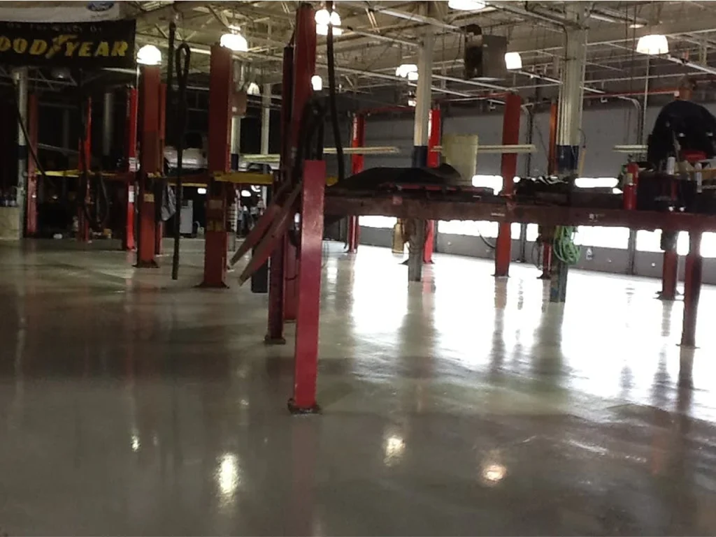 Automotive service garage with vehicle lifts and freshly coated epoxy flooring, reflecting overhead lighting.