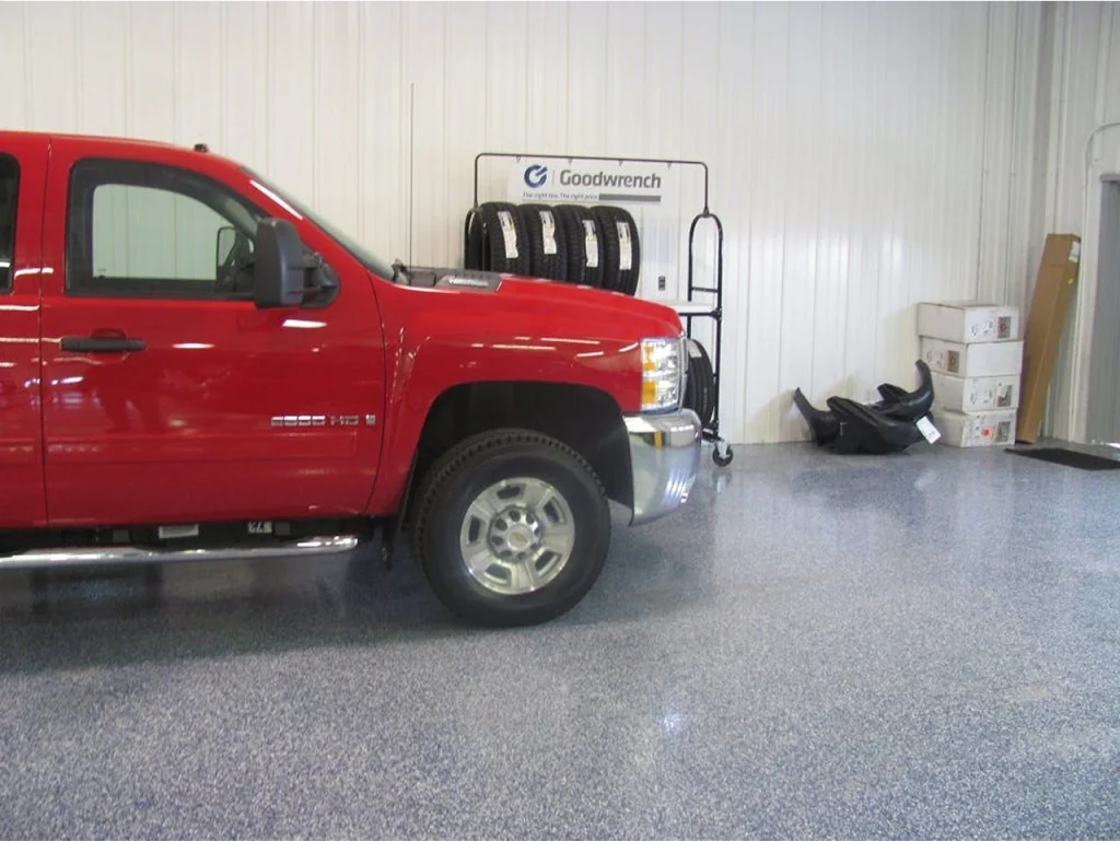 Worker applying decorative epoxy flake flooring in an auto service bay, with part of the floor completed and part still being coated.
