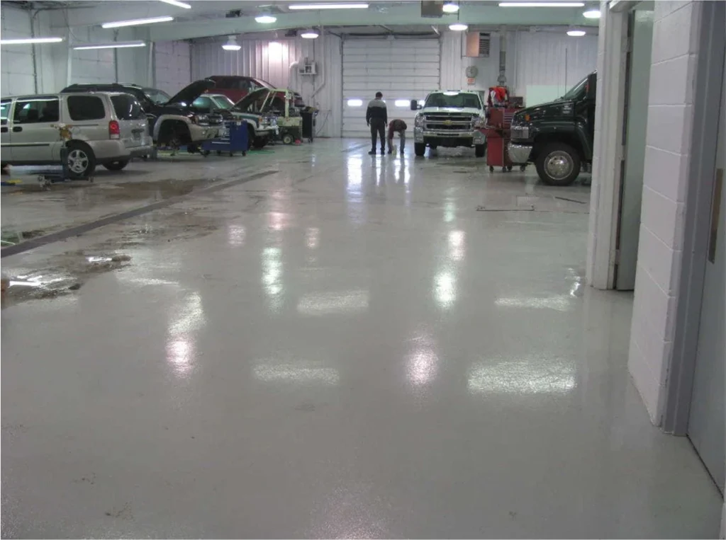 Auto service garage during floor resurfacing, with equipment and workers preparing concrete for epoxy coating.