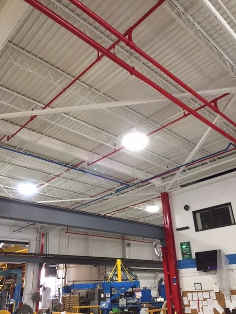 Finished ceiling after cleaning and coating—bright white deck with red fire-sprinkler piping and tidy, illuminated production area below.