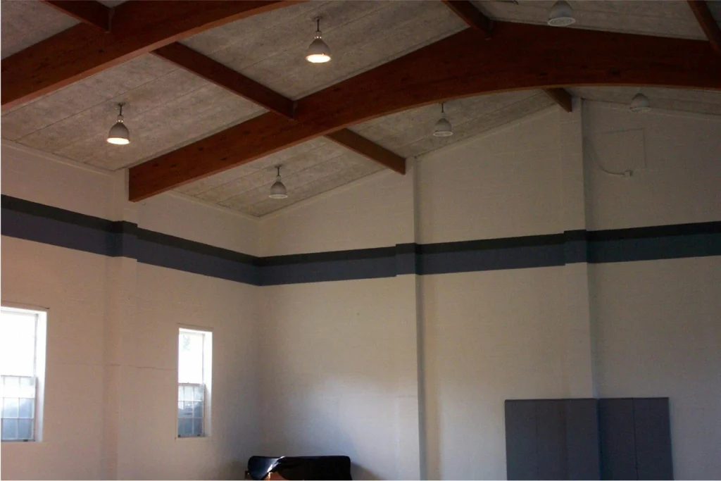 Church interior with wood-beam ceiling, white walls, and accent paint stripe, lit by hanging pendant lights.