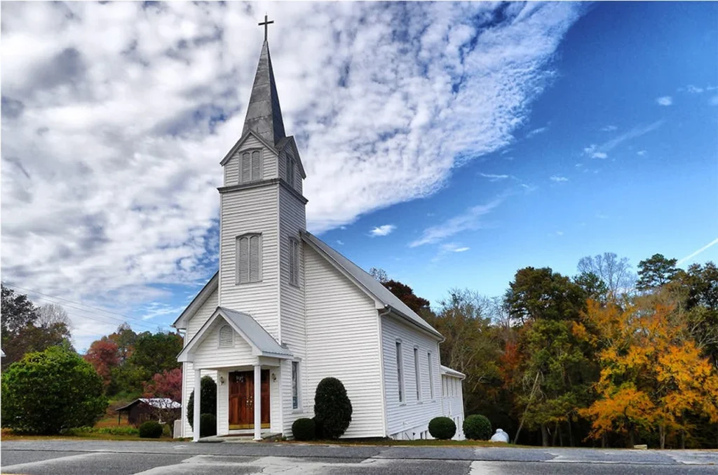 Exterior of a traditional brick church with steep gabled roof, photographed under a clear blue sky.