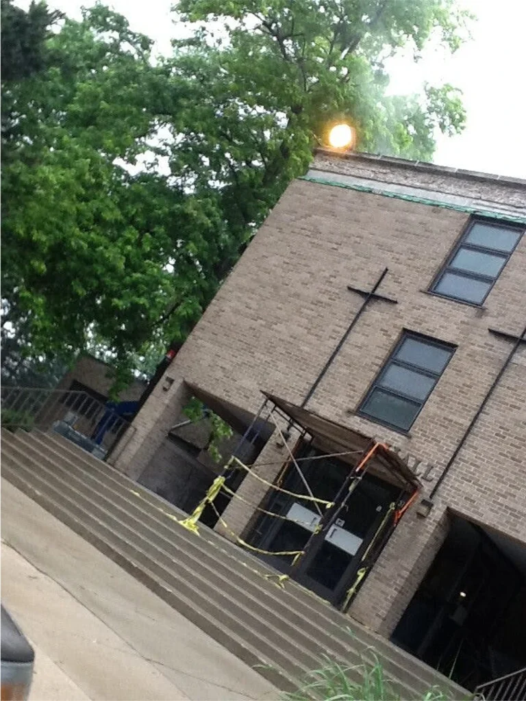 Church sanctuary interior with rows of wooden pews, stained glass windows, and hanging pendant lights.