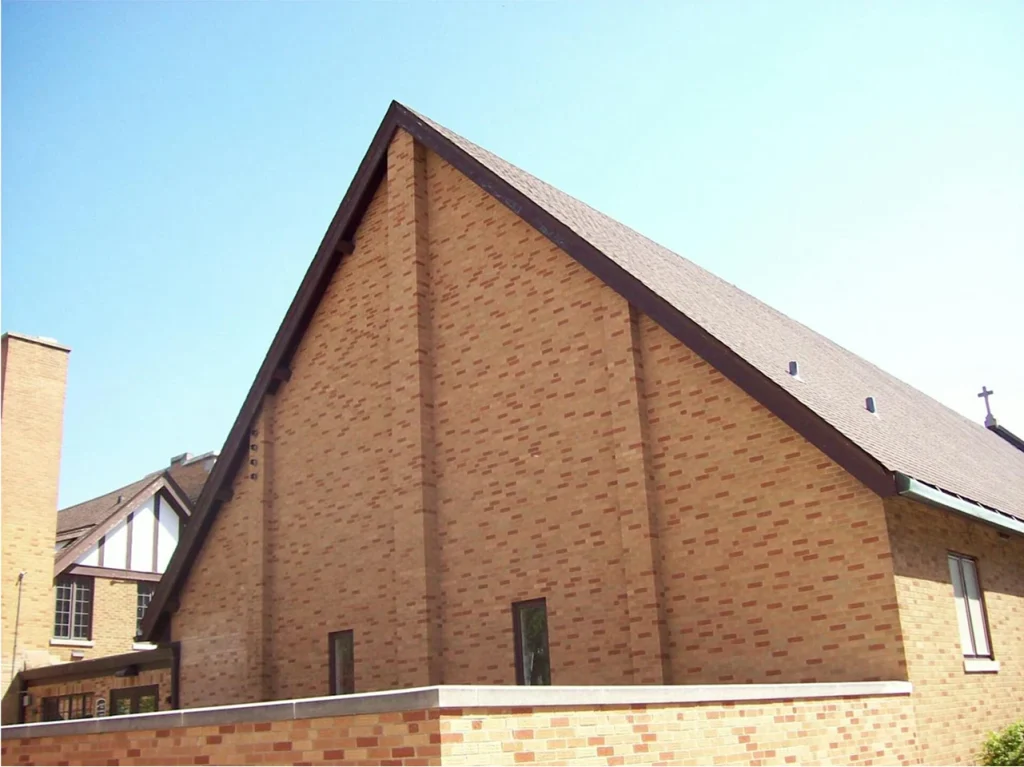 Large brick church with tall gabled roof, photographed from the side against a bright sky.