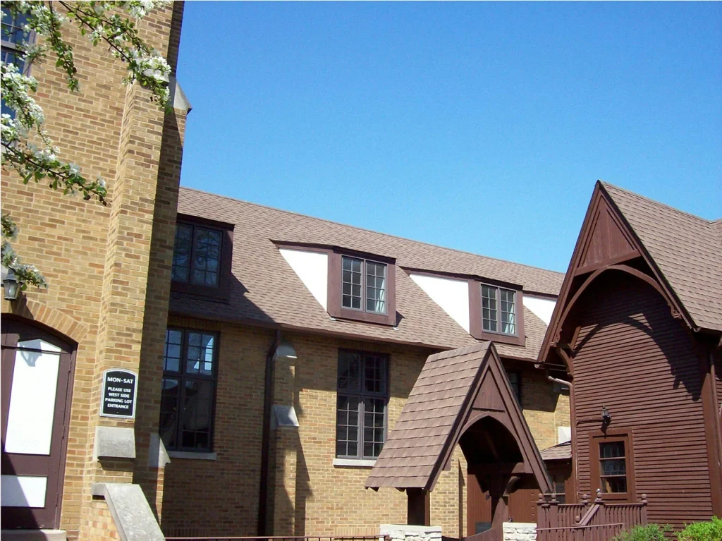White wooden church with steeple and cross, set against a partly cloudy sky with trees in the background.