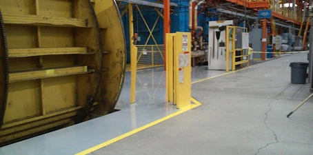Factory or industrial facility with large yellow machinery, polished concrete flooring, and safety lines marking walkways.