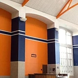 Large commercial interior with tall walls painted in bold orange and navy blue accents, featuring high ceilings and natural light from tall windows.