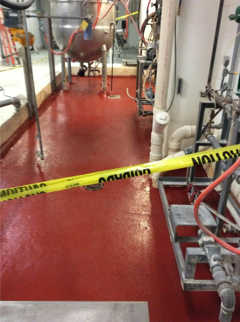 Completed red urethane-cement style floor in a processing area; fresh surface cordoned off with caution tape.