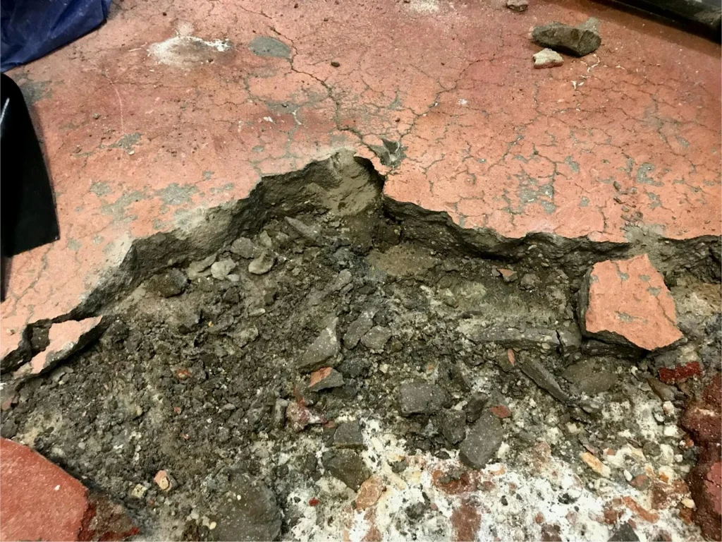 Severely spalled red floor coating with loose aggregate and cracked concrete beneath.