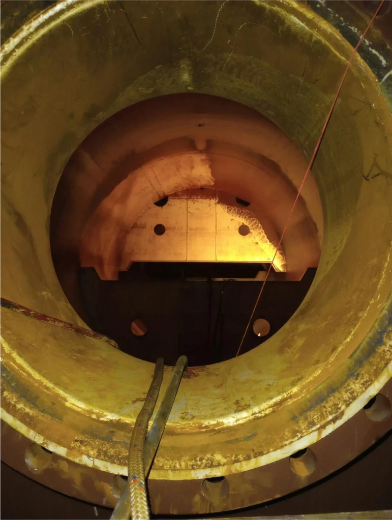 View through a tank manway showing a partially cleaned interior surface with lifelines running inside.