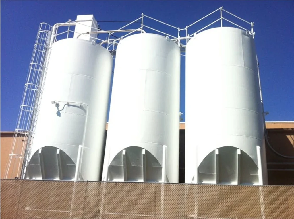 Same trio of silos after rehabilitation, all uniformly repainted bright white with clean ladders and railings.