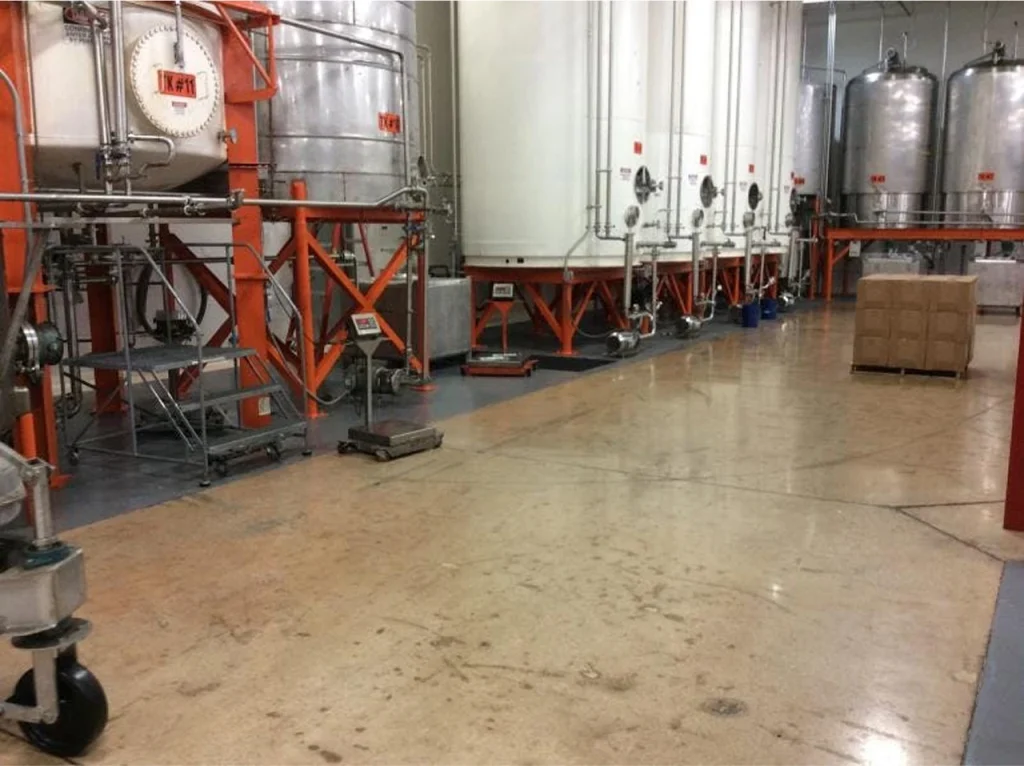 Industrial food processing plant with large stainless steel tanks, orange support frames, and concrete flooring.