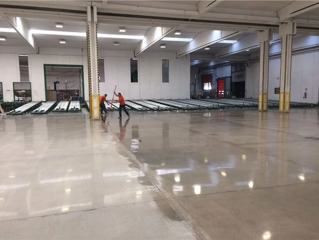 Two workers applying finish to a polished concrete floor inside a large food production facility.