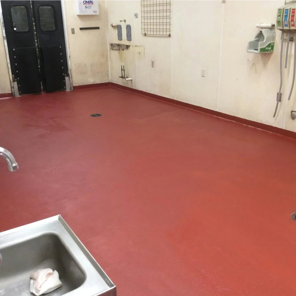 Food processing prep room with seamless red epoxy flooring, stainless steel sink, and wall-mounted sanitation equipment.