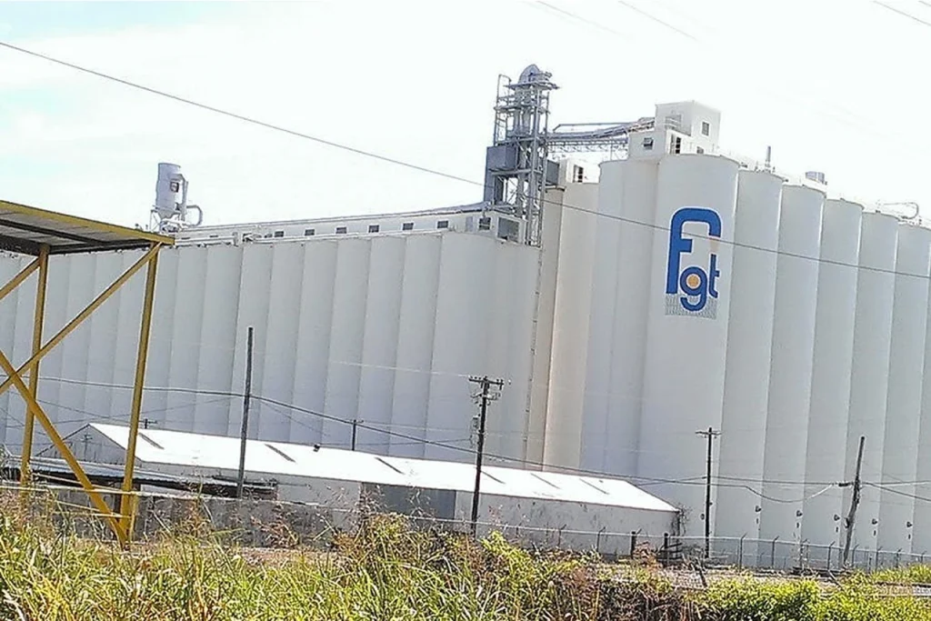 Large white grain silos with industrial piping and equipment at a food processing facility.