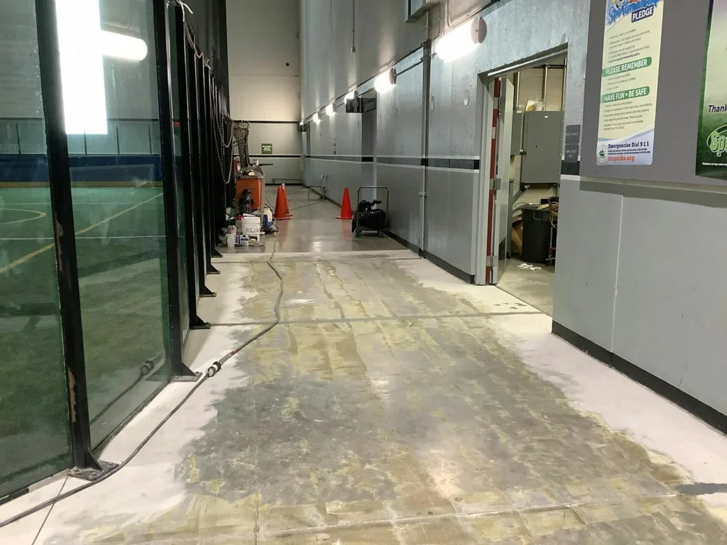 Sports corridor before: scraped, patchy concrete with equipment and cables along glass wall.