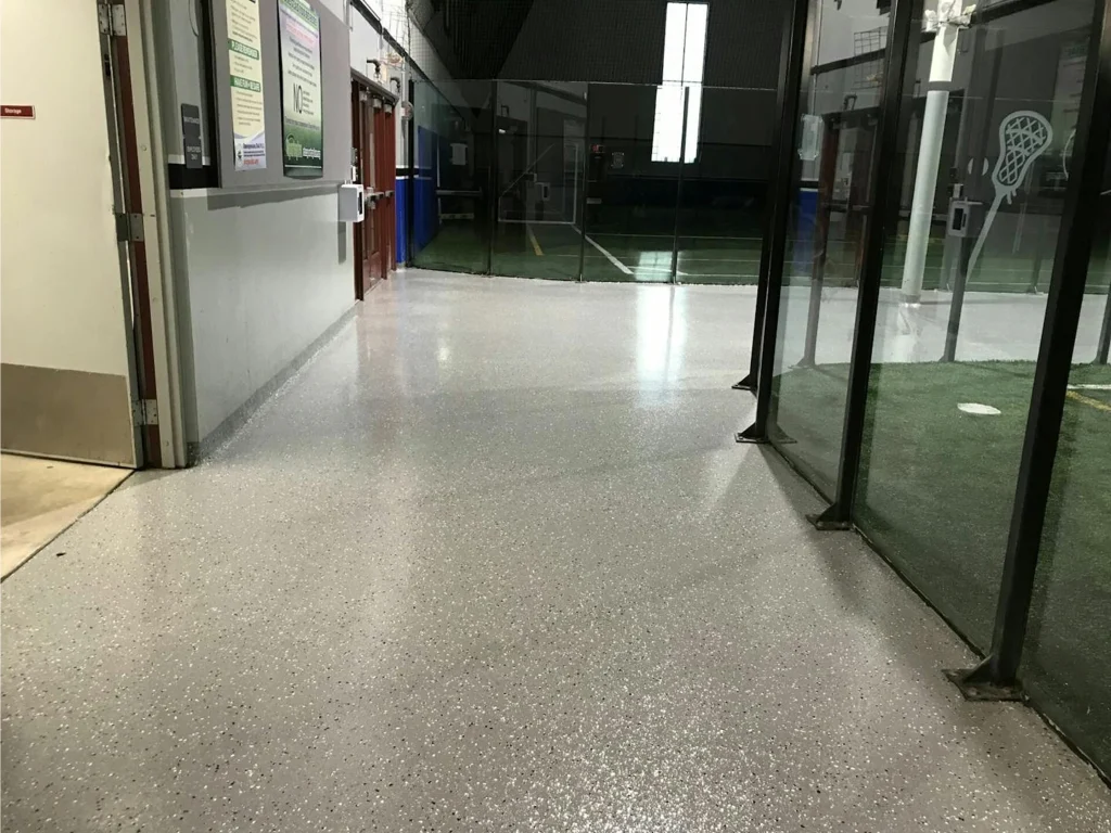 Sports facility corridor after: light gray flake epoxy alongside indoor turf behind glass panels.
