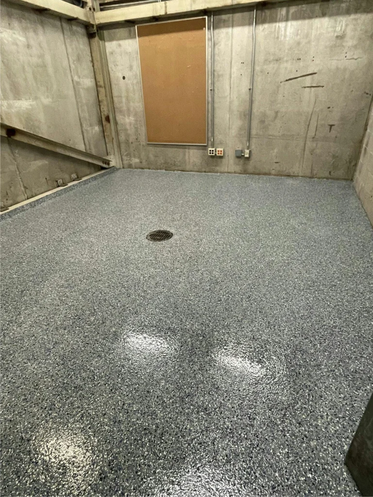 Small utility room after coating: speckled gray epoxy floor with central drain, walls unfinished.