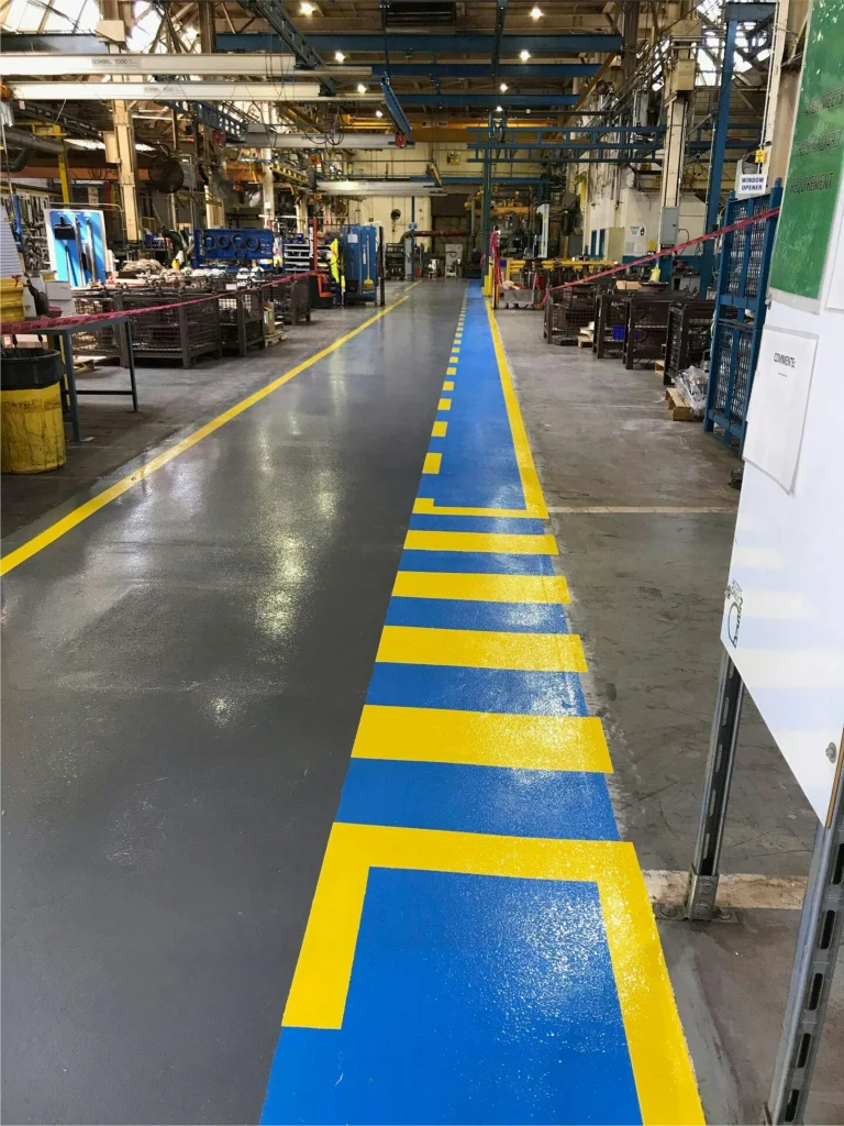 Production area after striping: gray floor with blue pedestrian lane and bold yellow safety markings.