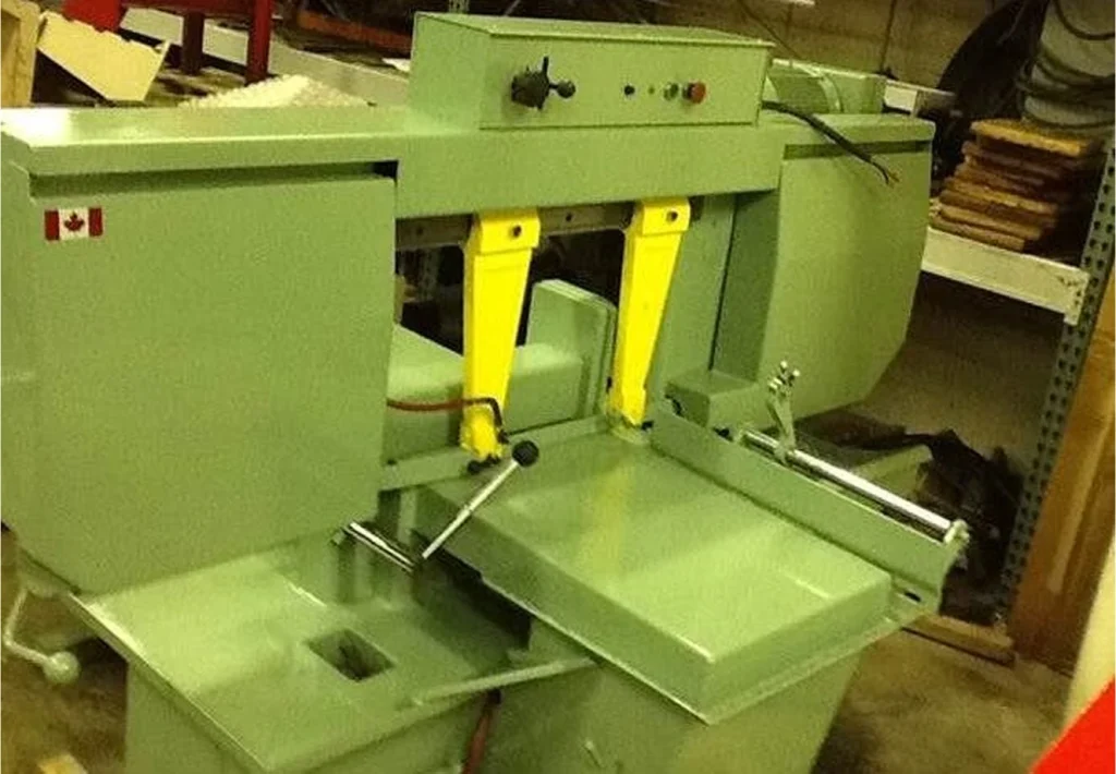Metal bandsaw after refurbishment, freshly painted green with bright yellow blade guards and clean tables.