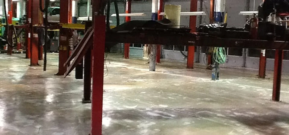 Auto service bay with red steel posts and tools suspended overhead, showing a smooth concrete floor reflecting light across the work area.