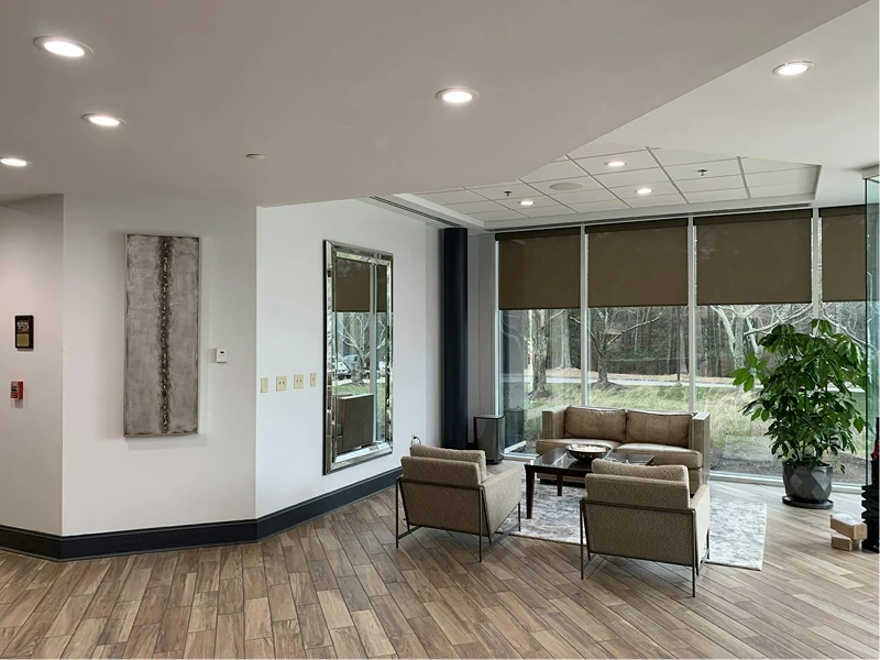 Sunlit lounge area with large windows and views of trees outside. Neutral wall colors, dark baseboards, and coordinated seating on a rug showcase a recently painted, welcoming office corner.
