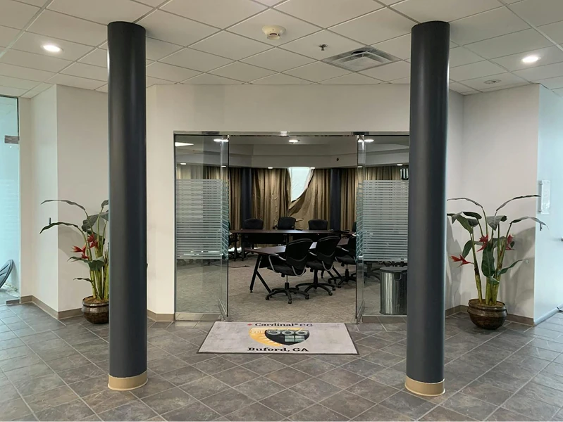 Entrance to a conference room framed by two dark columns and glass doors with frosted bands. Neutral gray walls and tiled floor highlight the clean, newly painted office environment.