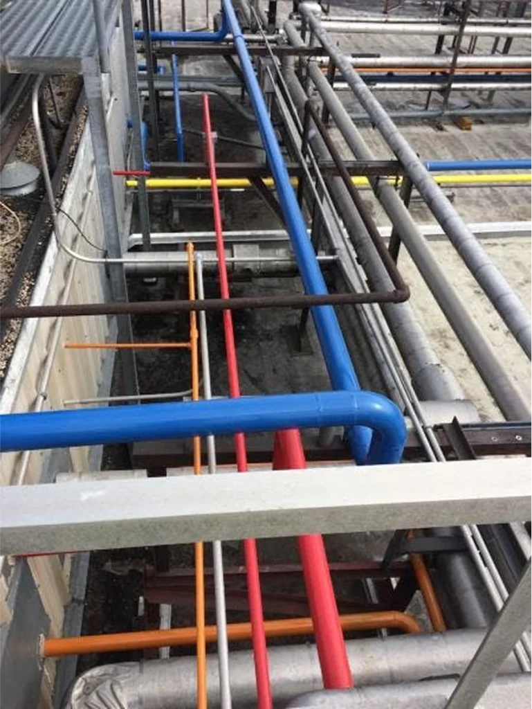 Overhead view of roof service pipes painted blue, red, yellow, and orange running through a conduit rack.