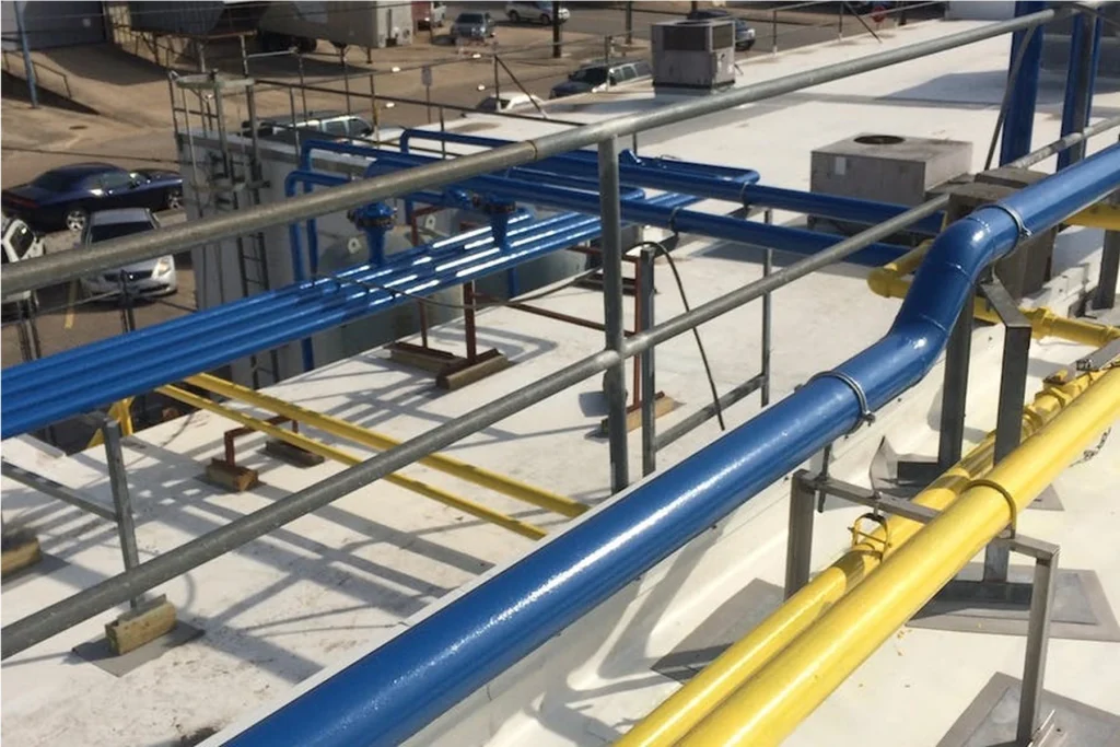 Close-up of rooftop blue and yellow painted pipes on metal supports behind a safety railing.