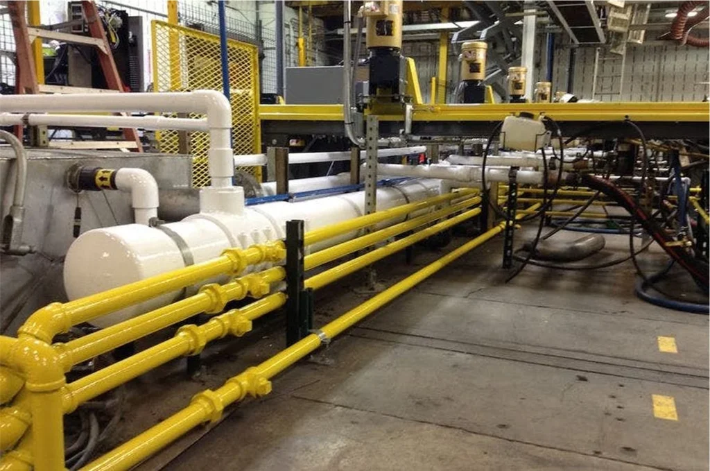 Factory mechanical area with a white cylinder and several parallel yellow pipes on stands along the floor.