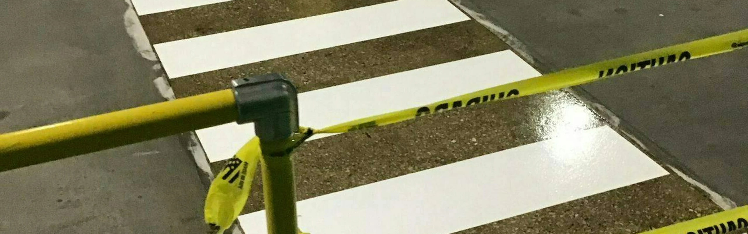 Newly painted white pedestrian crosswalk stripes on factory concrete, cordoned off with yellow caution tape.