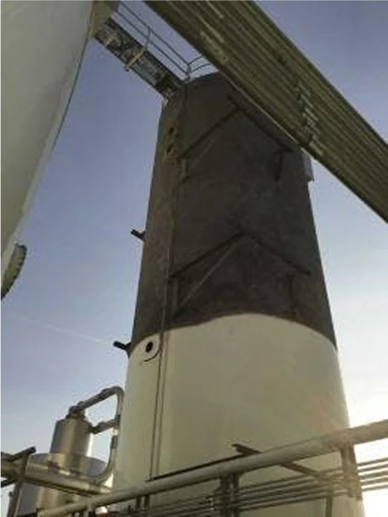 Tall vertical tank mid-project shows a sharp line between freshly cleaned white coating below and dark, sooty surface above.
