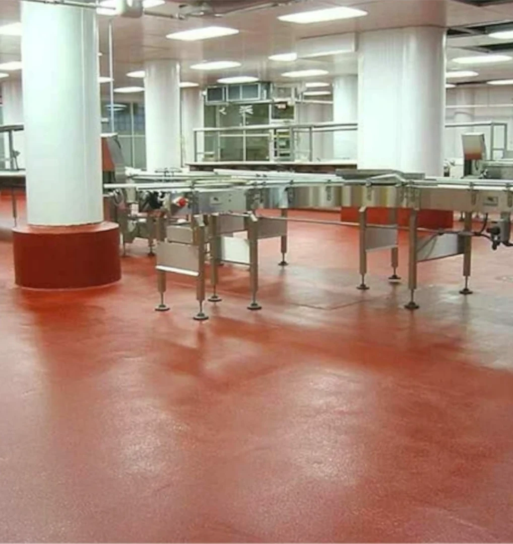 Bright, clean production room featuring a seamless red epoxy floor, white columns, and stainless steel conveyor equipment under evenly spaced ceiling lights.