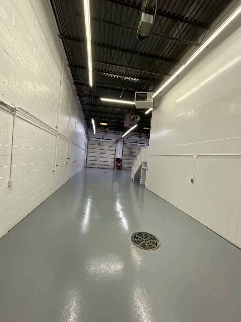 Same industrial bay with freshly coated glossy gray floor and white walls, leading to a roll-up door.