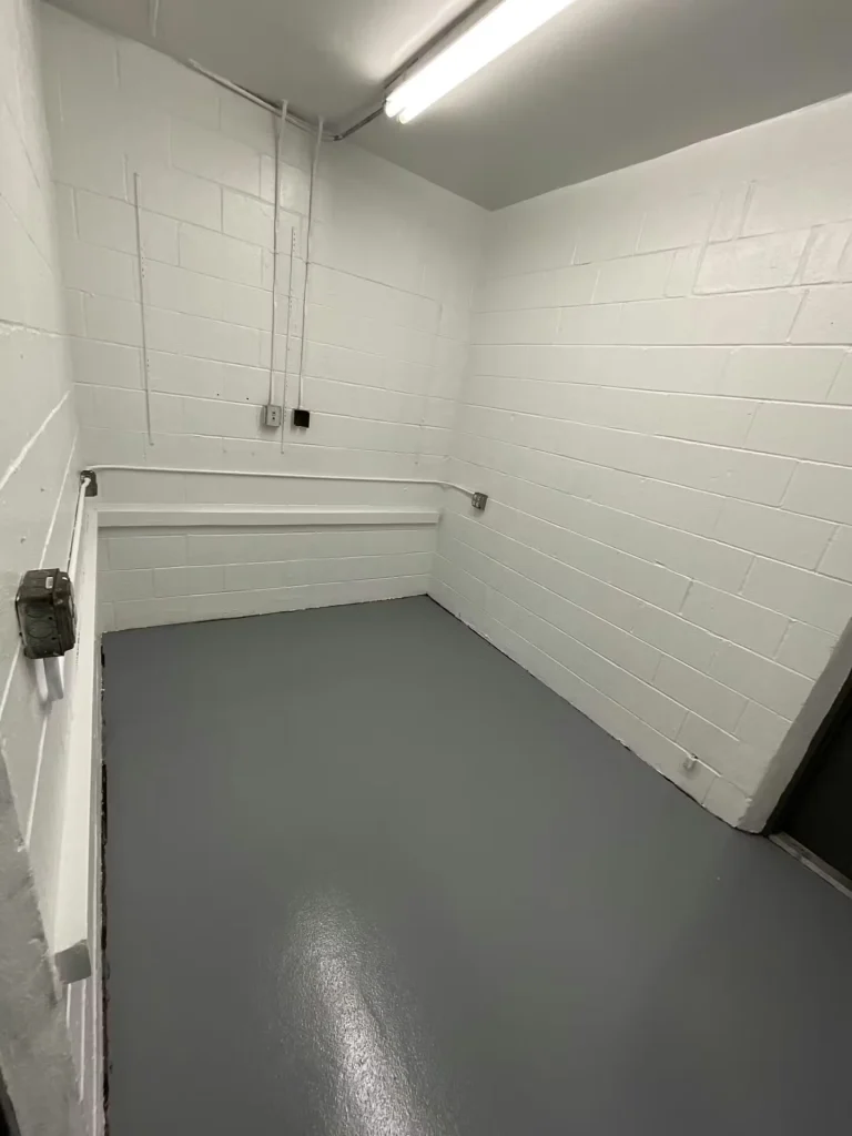 Small utility room with white walls and a smooth gray coated floor, showing conduit along the wall.