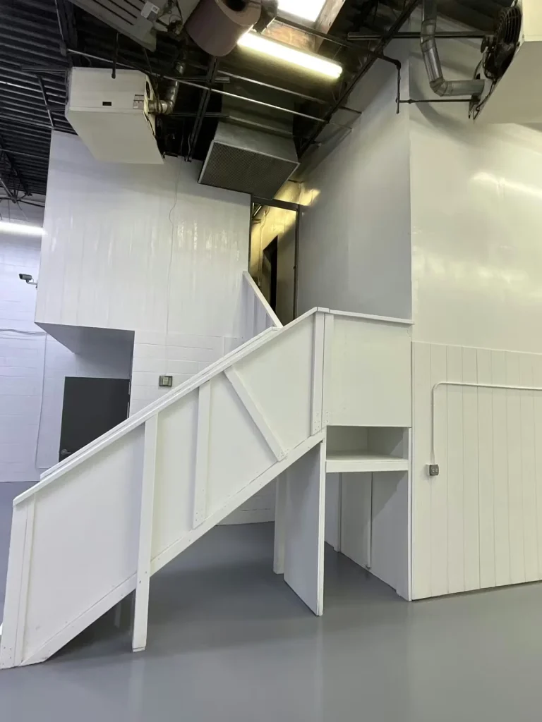 Refreshed warehouse stairs and mezzanine painted white above a glossy gray floor, with exposed ceiling ductwork overhead.