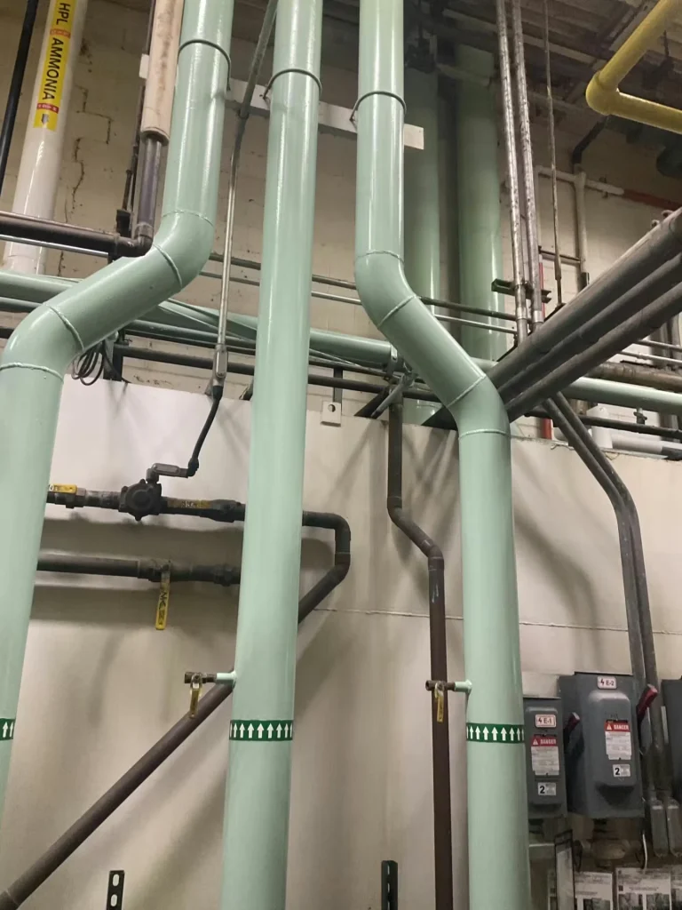 Tight view of a machinery cluster with large grey electrical control boxes labeled “6” and “7,” multiple hanging cables, yellow cylindrical vessels, and blue pump components with handwheels and pressure gauges.