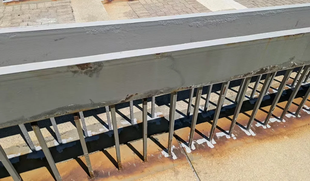 Wider view of the same outdoor handrail section cordoned off with yellow caution tape tied to an orange traffic barrel; parking lot and landscaping visible beyond.