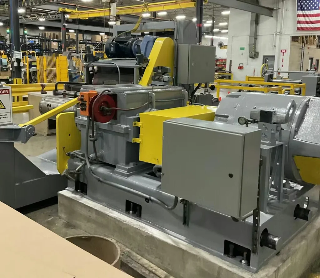Large industrial machine painted gray and yellow inside a factory area, with safety railings and equipment surrounding it.