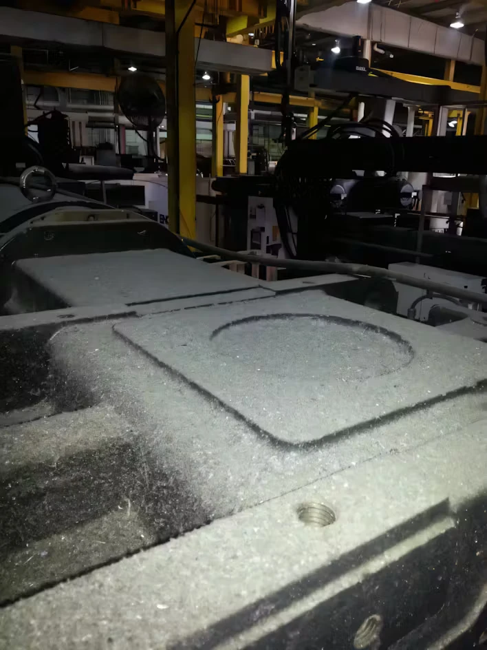 Close-up of dusty industrial machinery in a factory setting, with yellow support beams and equipment in the background under overhead lights.