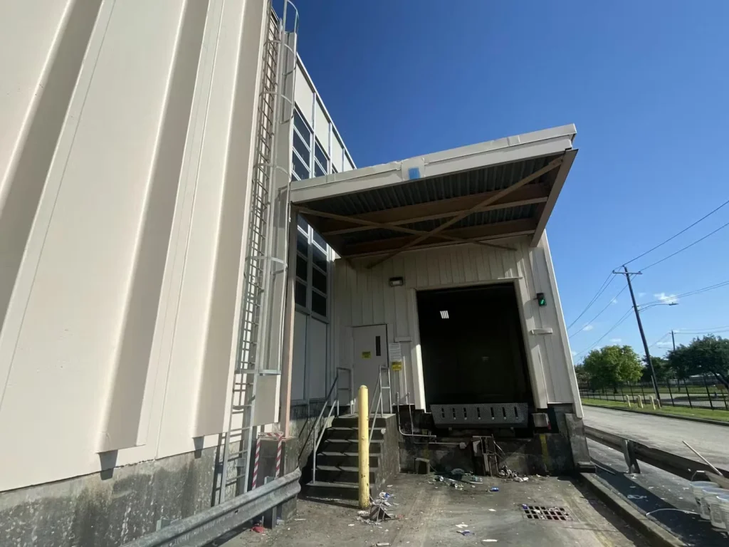 Warehouse loading dock facade with multiple doors and a ramp, framed by a partly cloudy sky.