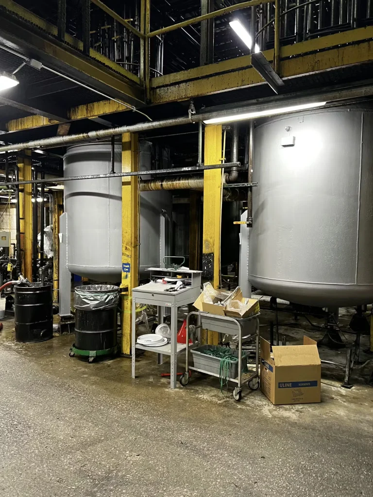 Cleaned industrial space with freshly painted gray tanks and bright yellow support columns under overhead catwalks.