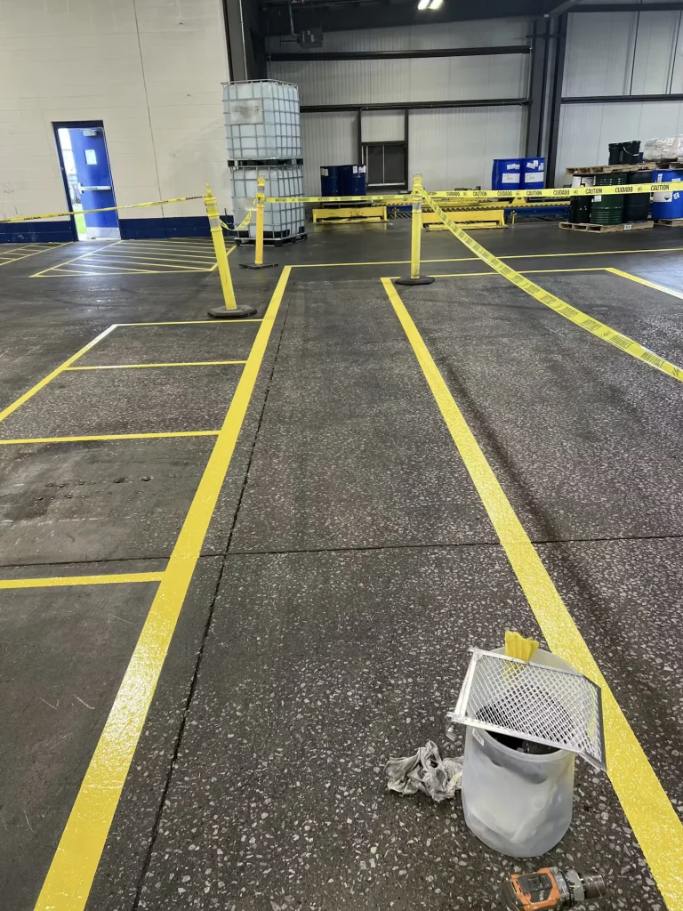 Fresh yellow floor striping marking work zones, cordoned off with caution tape, with paint bucket and tools nearby.