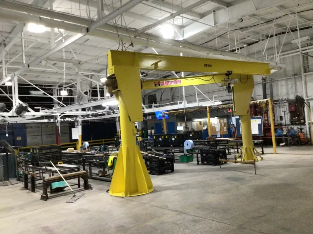 Large open shop floor with a yellow overhead jib crane and painted white ceiling structure; drums and carts sit in the foreground.