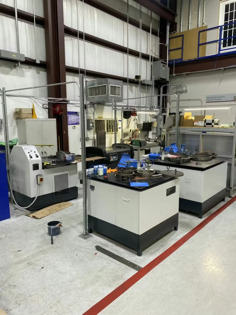 Tall white industrial cabinet-style machine with a side control panel and hoses, positioned next to a metal roll-up door; a red floor line marks the edge of the work area.