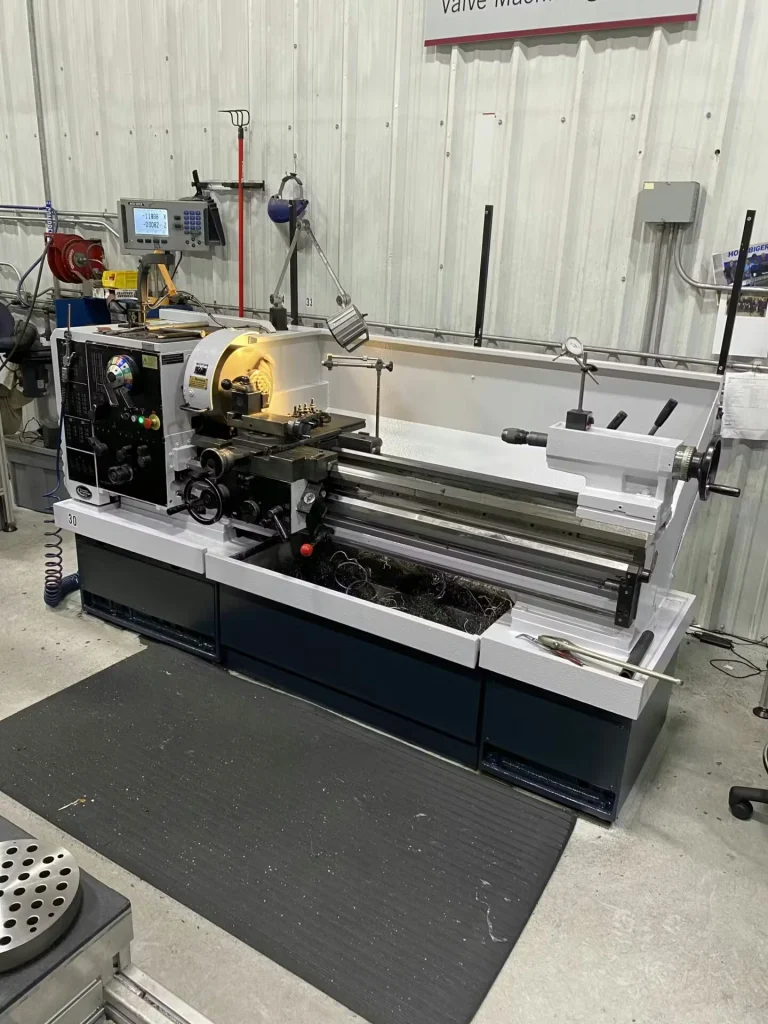 Large “KINGSTON” heavy-duty lathe with a large faceplate and green steady rest; red floor line runs along the aisle in front, with other machines and worktables nearby.