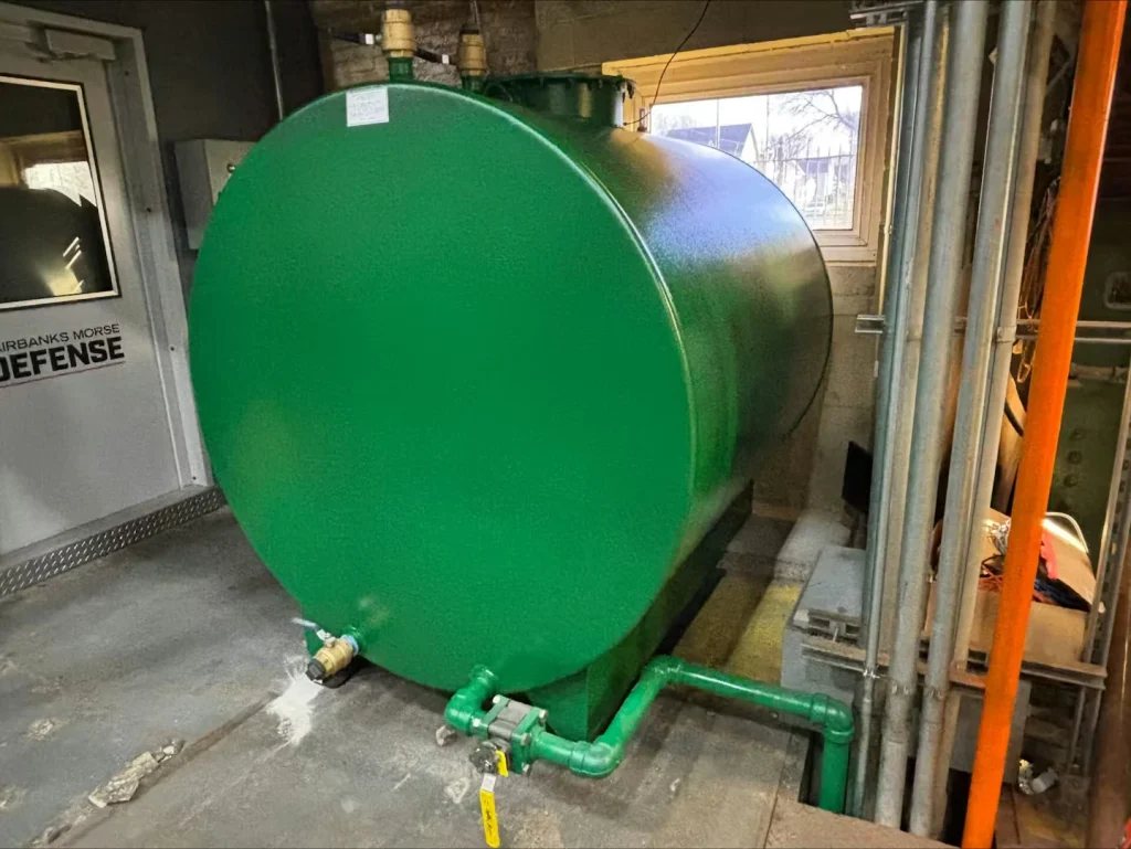 Large horizontal cylindrical tank painted green inside a utility room, with green piping and a shutoff valve connected at the base near a door and window.