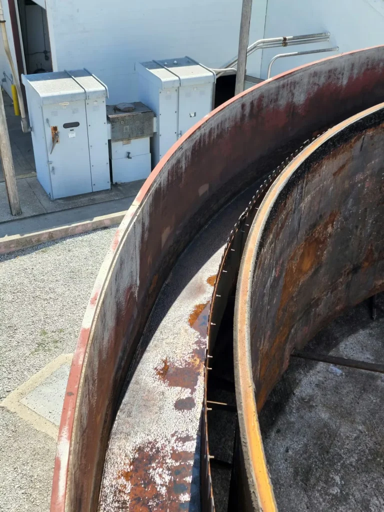 Two large curved steel ring sections with heavy surface rust, staged outdoors near white electrical cabinets and conduit.