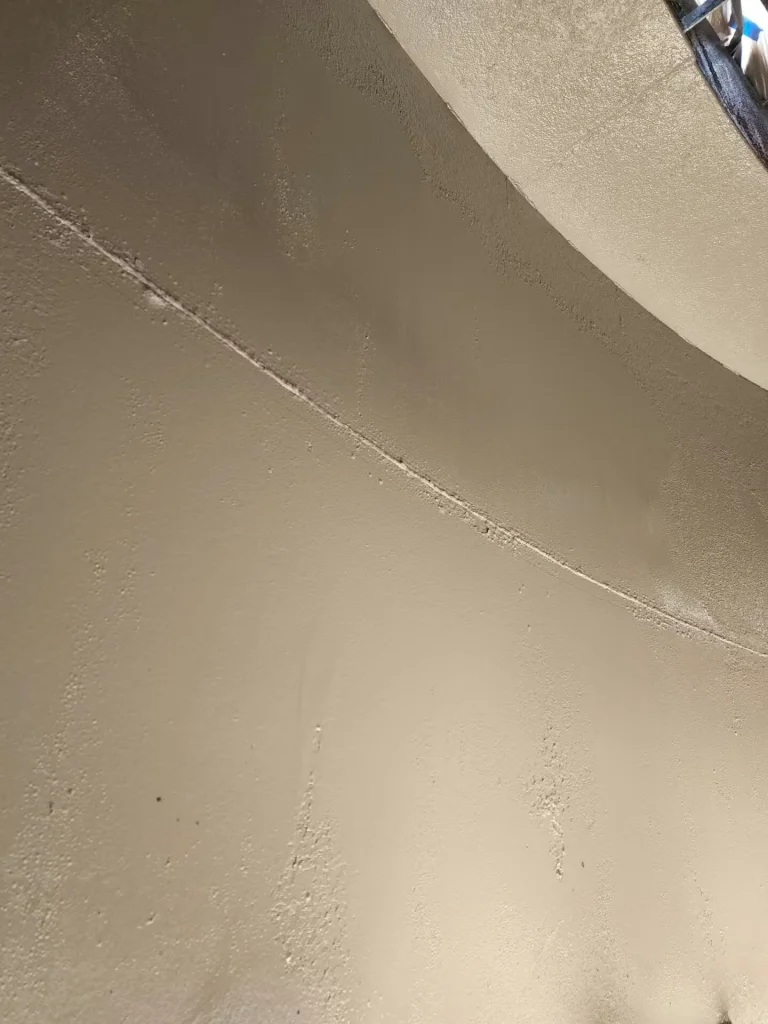Close-up of a beige/cream freshly coated curved tank interior, with a weld seam running across the surface and visible spray texture.