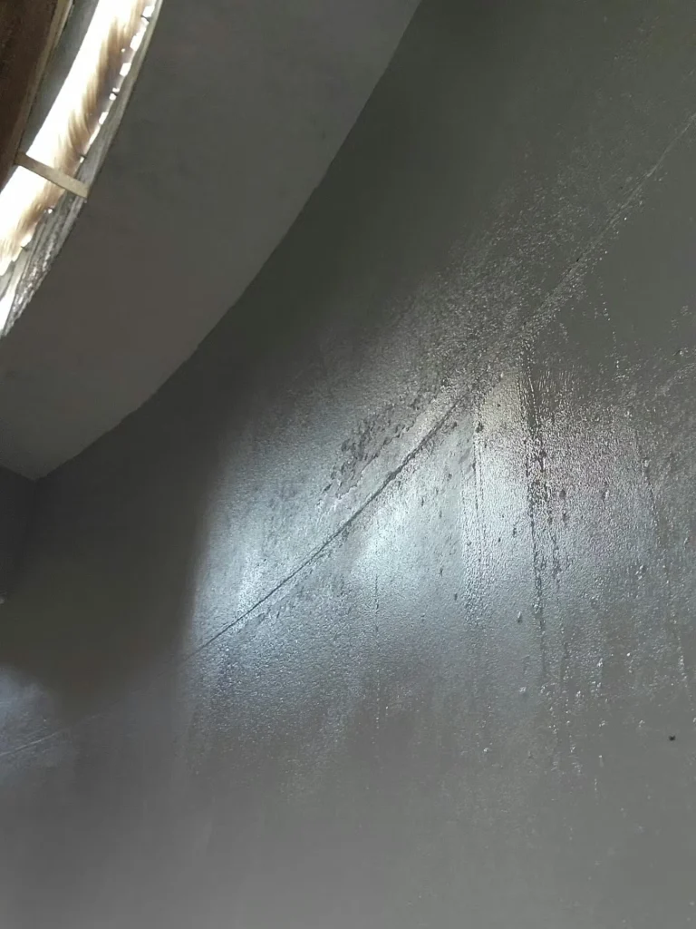 Dark gray, glossy-coated interior tank wall with streaks and a seam line, illuminated by bright light from an opening at the upper left.